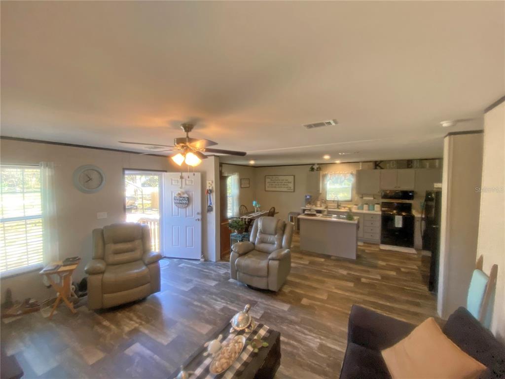 An open-concept living room and kitchen featuring wood-look flooring, a ceiling fan, and recliners — 203 SW 5TH AVENUE, PALATKA, FL