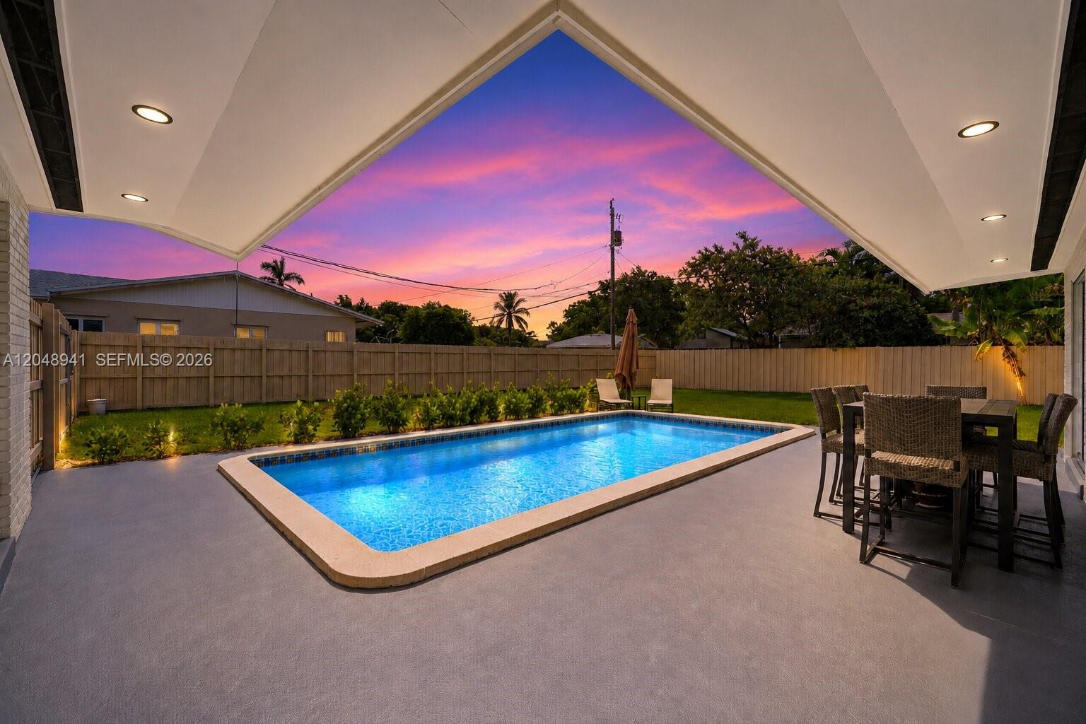 A rectangular swimming pool sits on a patio under a covered lanai at sunset — 19225 Bel Aire Dr, Cutler Bay FL 33157, CUTLER BAY, FL