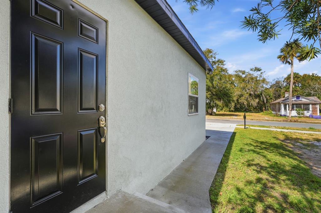A black exterior door on a light-colored stucco wall next to a concrete walkway — 557 LIVE OAK AVENUE, DAYTONA BEACH, FL