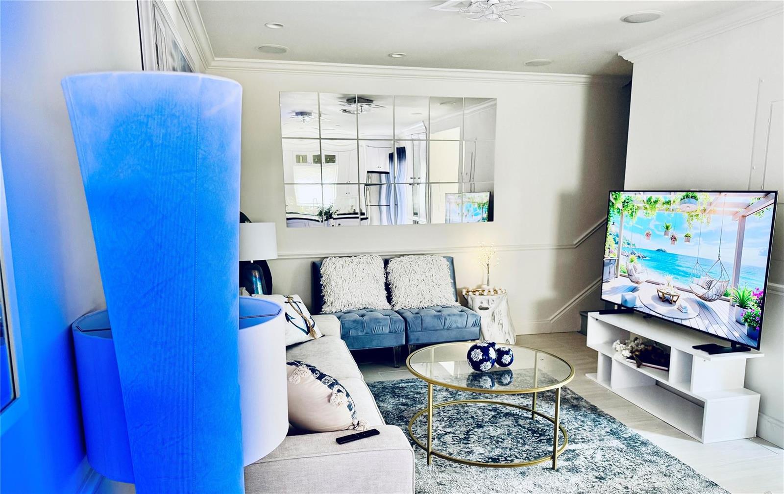 A living room features a beige sofa, blue accent chairs, a glass coffee table, and mirrors — 1010 NE 8th Avenue # 31f, Delray Beach FL 33483, DELRAY BEACH, FL