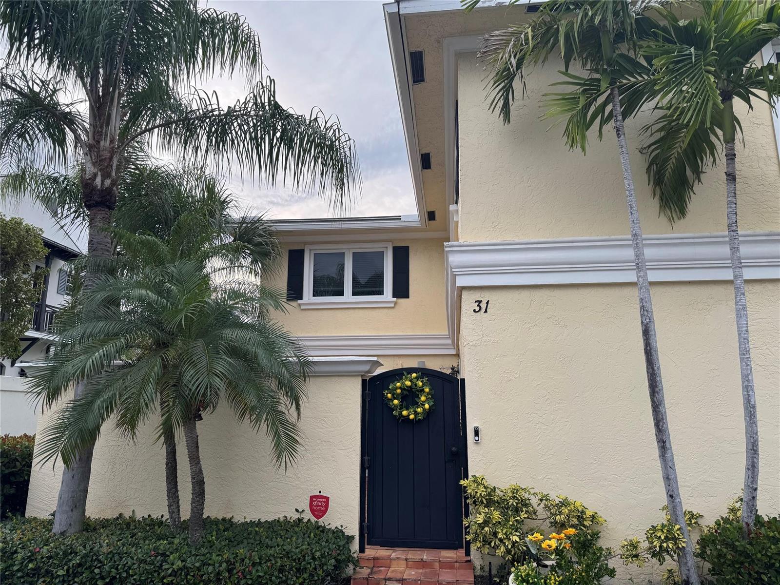 A yellow two-story house exterior features a black gate with a lemon wreath and palms — 1010 NE 8th Avenue # 31f, Delray Beach FL 33483, DELRAY BEACH, FL