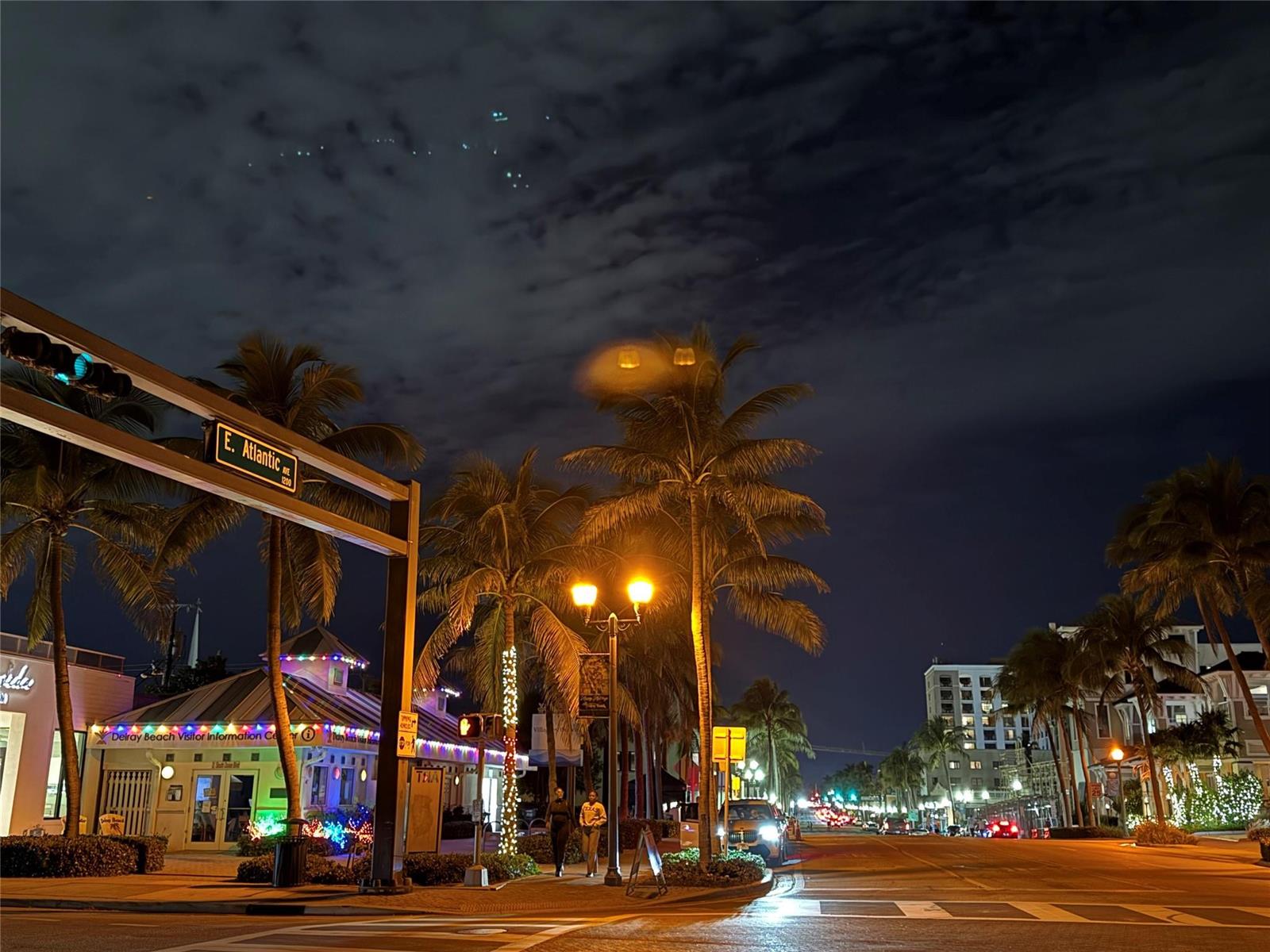 A night view of a street intersection with palm trees, streetlights, and a visitor center — 1010 NE 8th Avenue # 31f, Delray Beach FL 33483, DELRAY BEACH, FL
