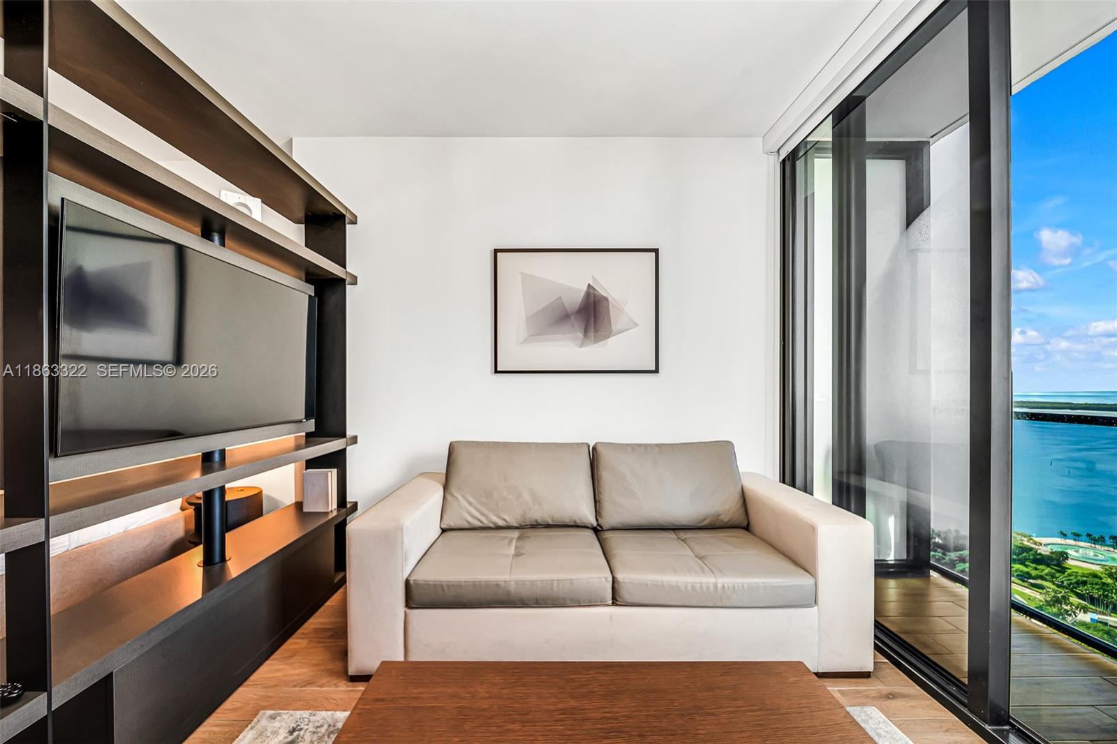 A living room features a sofa, a wall-mounted television, shelving, and a balcony with water views — 398 NE 5 # 4416, Miami FL 33132, MIAMI, FL