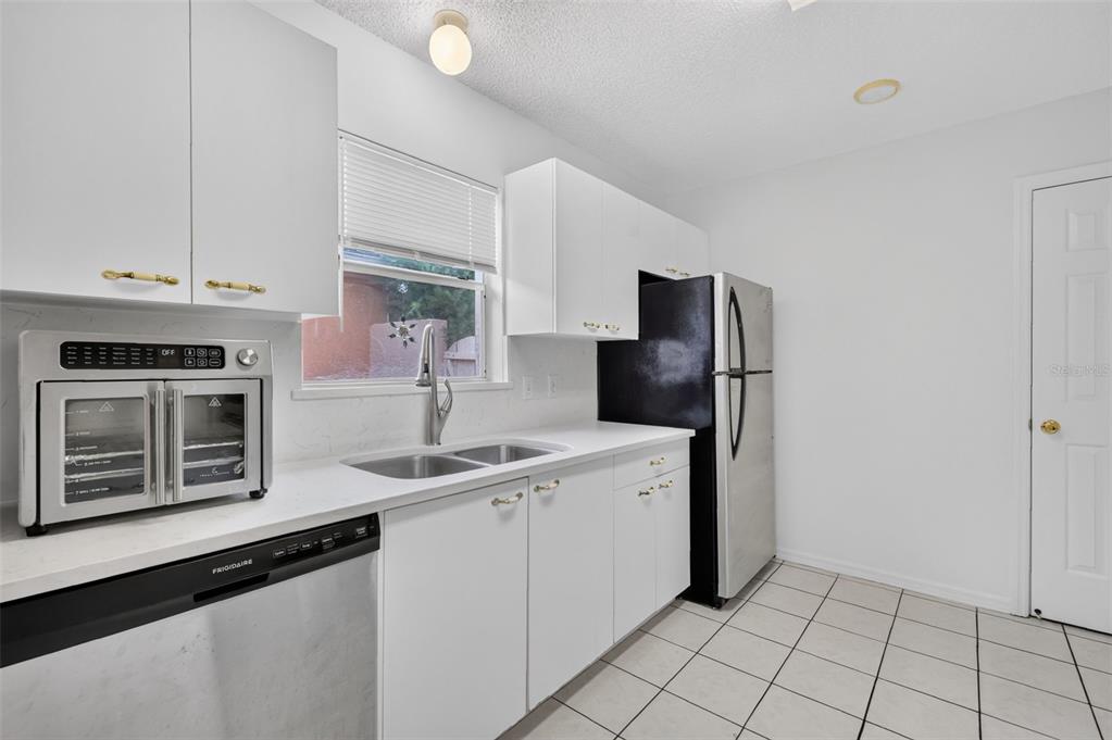 A kitchen with white cabinets, stainless steel appliances, a double sink, and white tile floors — 954 AVALON AVENUE, LADY LAKE, FL