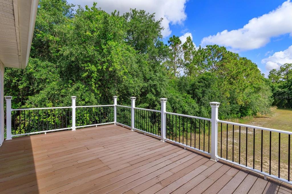 A wooden deck with white railings and black balusters overlooks a dense wooded area — 16201 CITRUS PKWY, CLERMONT, FL