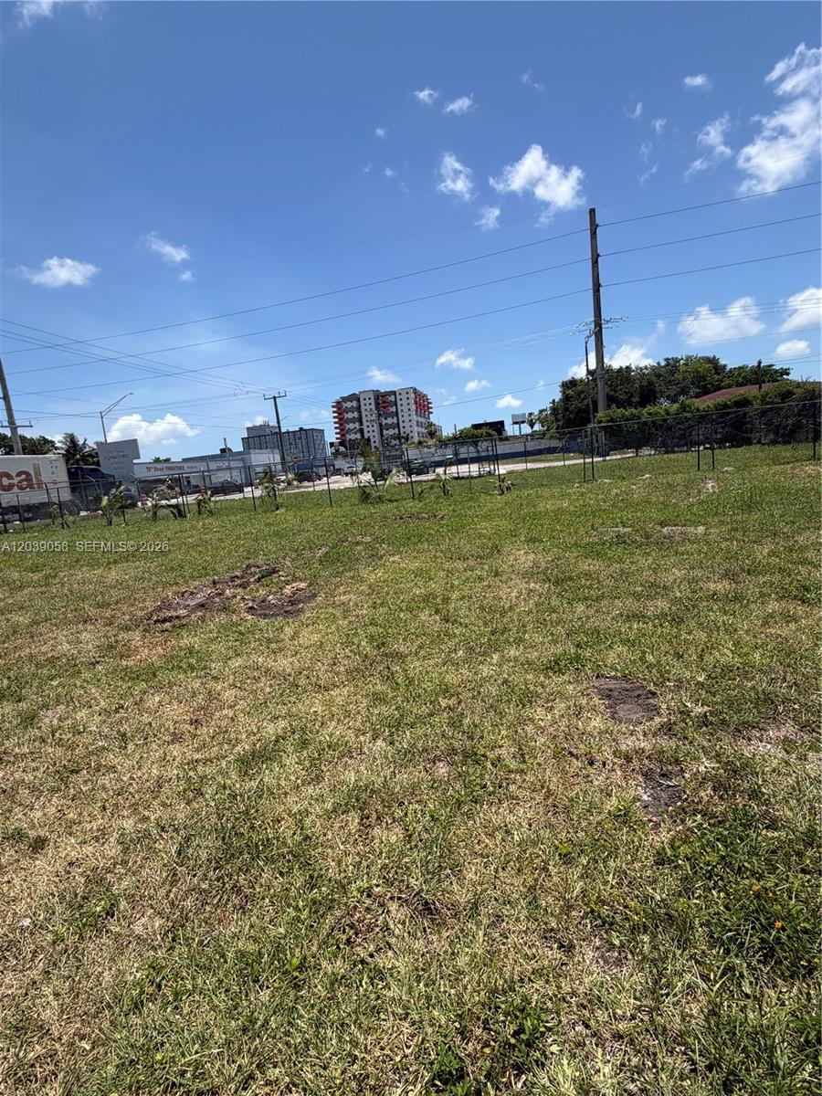 A grassy, vacant lot is enclosed by a chain-link fence under a bright blue sky — 810 NW 79th St, Miami FL 33150, MIAMI, FL