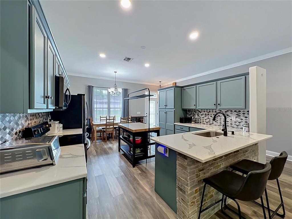 A kitchen features blue-green cabinetry, a white marble-topped island, and a brick-faced breakfast bar — 300 E GENEVA STREET, OCOEE, FL