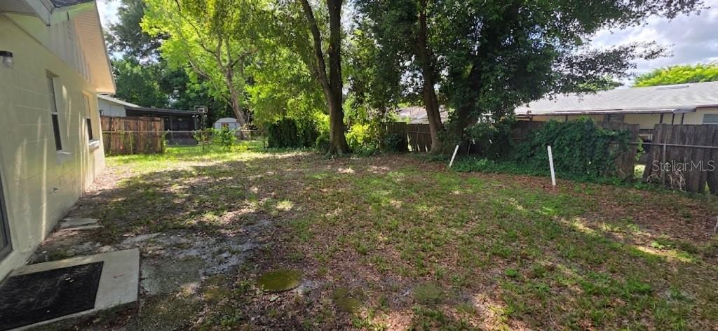 A backyard with a concrete patio, patchy grass, mature trees, and a wooden privacy fence — 7670 STRATFORD BOULEVARD, ORLANDO, FL