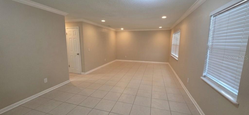 An empty room features light-colored tile flooring, beige walls, recessed lighting, and a window with blinds — 7670 STRATFORD BOULEVARD, ORLANDO, FL