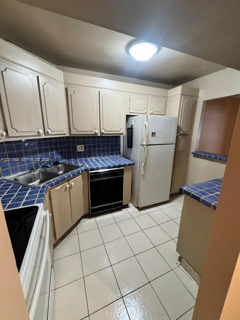 A kitchen features beige cabinets, blue tiled countertops, white appliances, and light-colored floor tiles — LAUDERHILL, FL