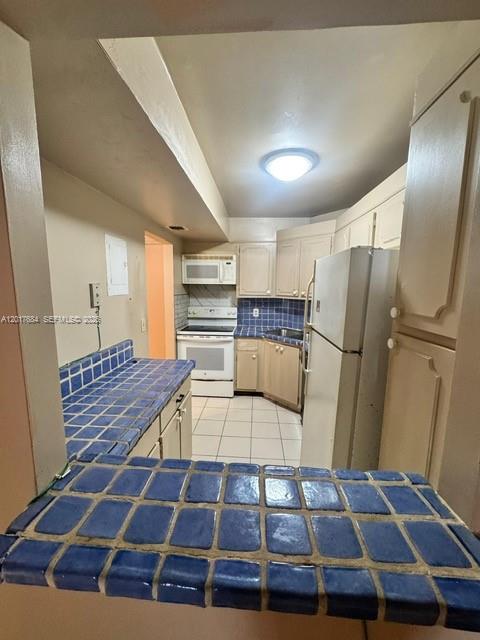 A kitchen features blue tiled countertops, white cabinets, a white refrigerator, and a tiled floor — LAUDERHILL, FL