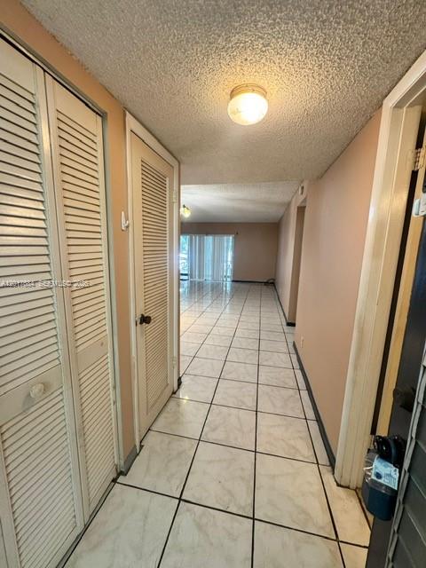 A hallway with white louvered closet doors, tiled floors, and a ceiling light fixture — LAUDERHILL, FL