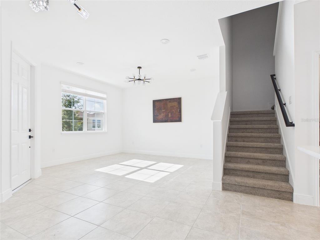 A bright, empty room features white walls, tile flooring, a staircase, and a modern chandelier — 5611 SW 72ND COURT, OCALA, FL