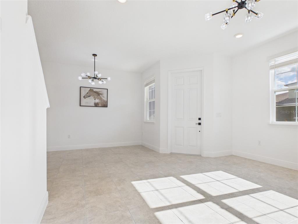A bright, empty room features white walls, tile flooring, two modern chandeliers, and two windows — 5611 SW 72ND COURT, OCALA, FL
