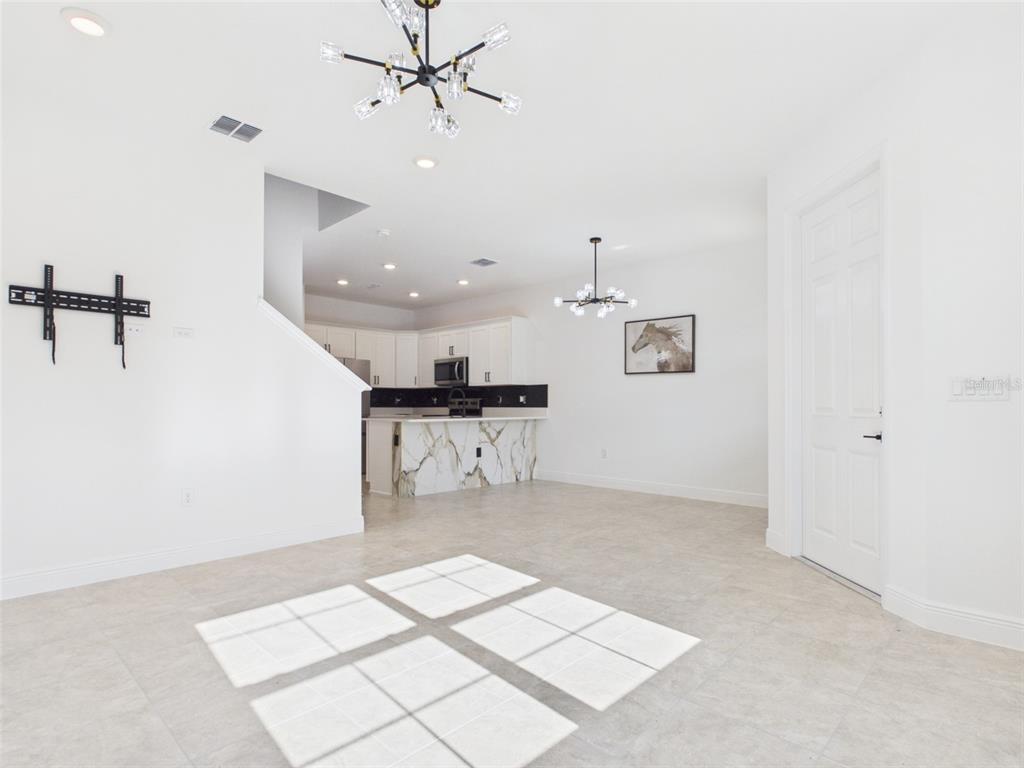 An open-concept living and dining area features a gray sofa, kitchen island, and modern chandeliers — 5611 SW 72ND COURT, OCALA, FL