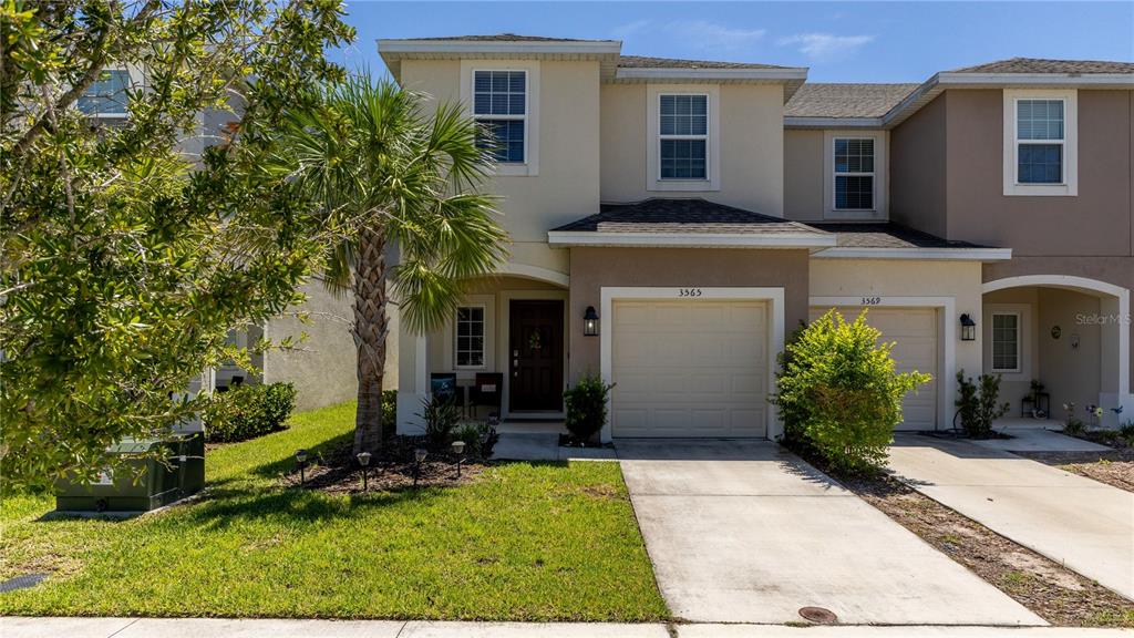A two-story townhouse with a beige stucco exterior, a single-car garage, and a palm tree — 3565 ANIBAL STREET, KISSIMMEE, FL