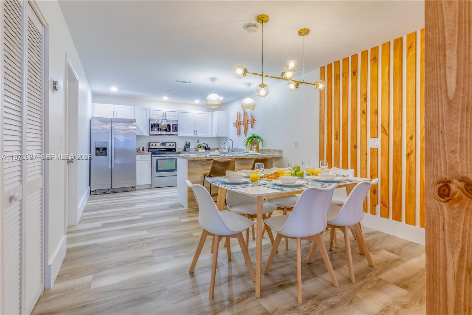 A dining area with a modern chandelier sits adjacent to a kitchen with white cabinetry — 1762 NW 15th St, Miami FL 33125, MIAMI, FL