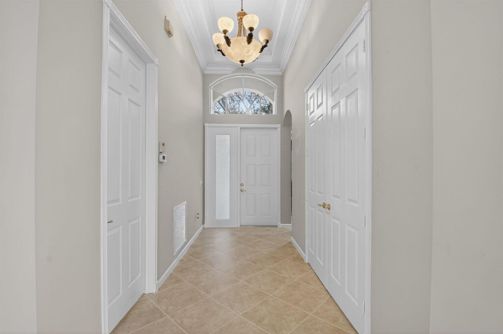 A bright entryway features a tiled floor, a chandelier, and a white front door — 7232 Morocca Lake Drive, Delray Beach FL 33446, DELRAY BEACH, FL