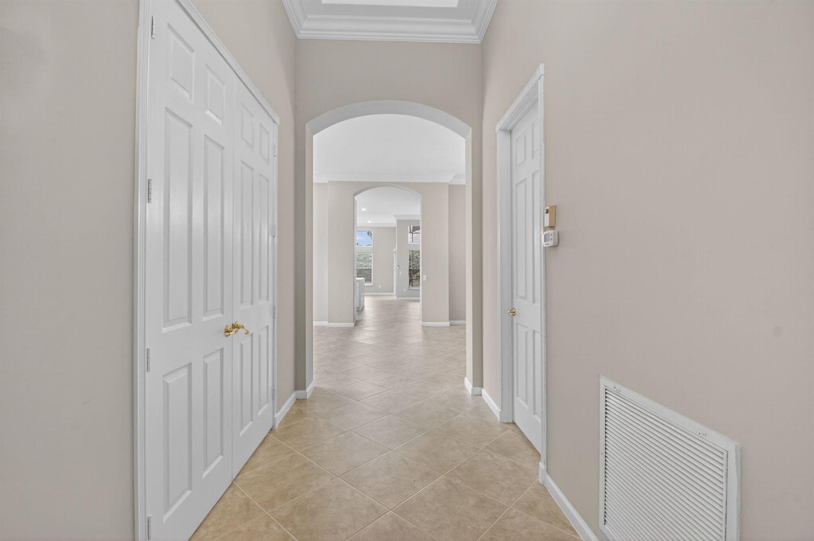 A hallway features beige tile flooring, arched doorways, and white paneled doors — 7232 Morocca Lake Drive, Delray Beach FL 33446, DELRAY BEACH, FL