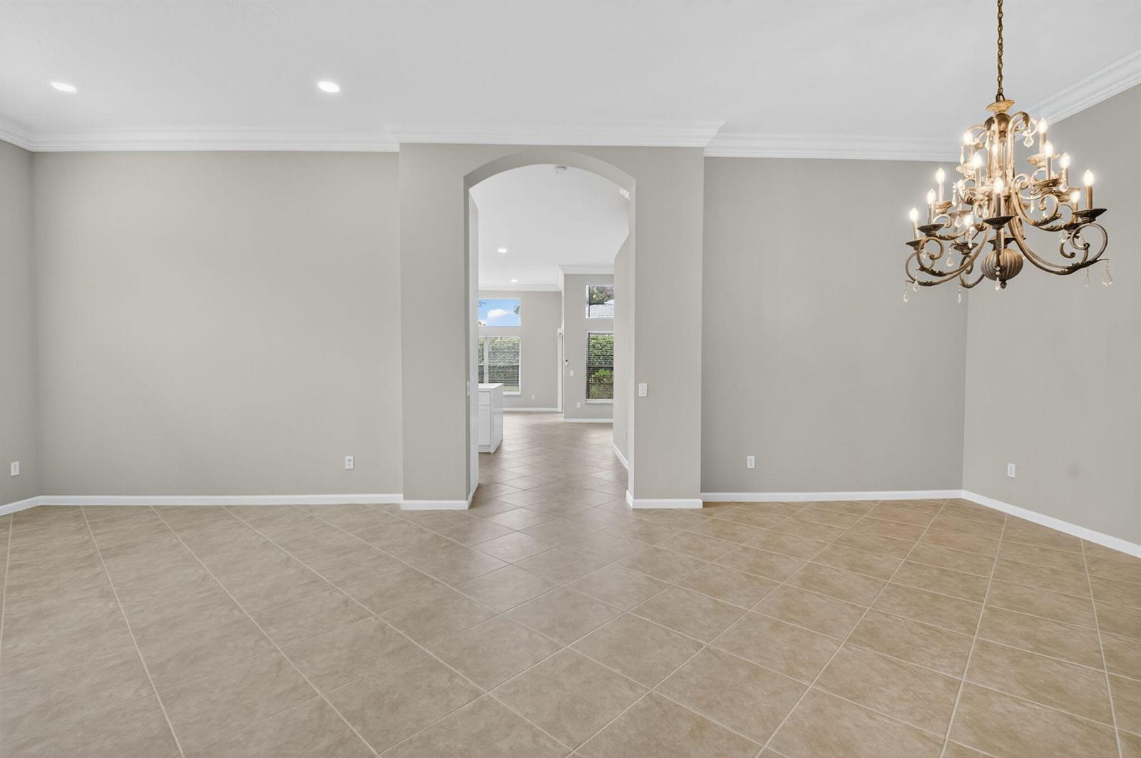 A dining room with tile flooring and a chandelier leads through an archway to a kitchen — 7232 Morocca Lake Drive, Delray Beach FL 33446, DELRAY BEACH, FL