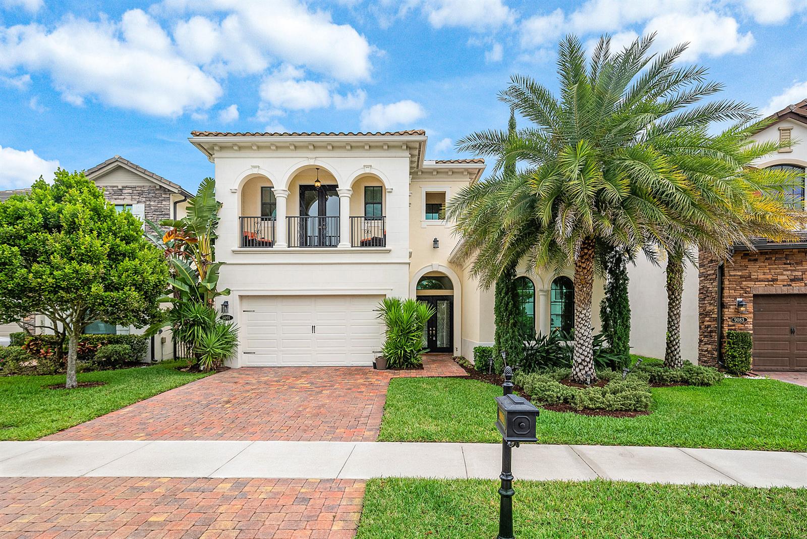 A two-story Mediterranean-style house with a brick driveway, a balcony, and a palm tree — 9091 Grand Prix Lane, Boynton Beach FL 33472, BOYNTON BEACH, FL