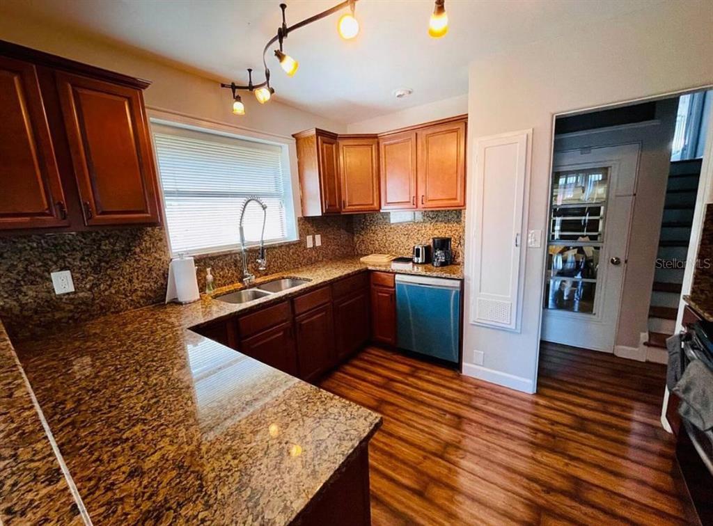 A kitchen features wood cabinets, granite countertops, a stainless steel dishwasher, and wood-look flooring — 582 REVILO BOULEVARD, DAYTONA BEACH, FL