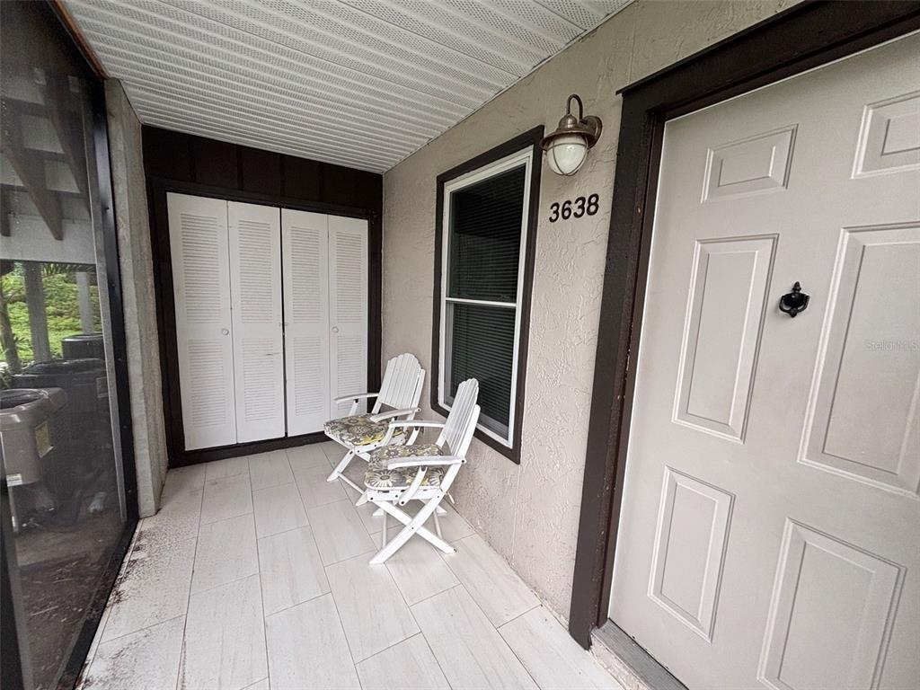A covered porch features white tiled flooring, two folding chairs, and a white entry door — 3638 59TH AVENUE W UNIT 3638, BRADENTON, FL