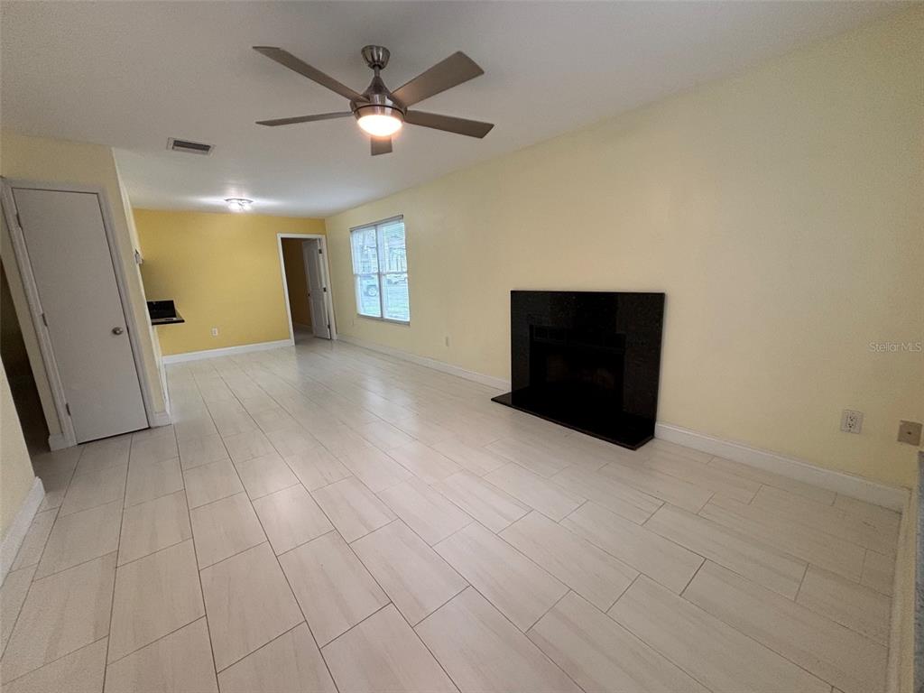 A living room with light-colored tile flooring, yellow walls, a ceiling fan, and a fireplace — 3638 59TH AVENUE W UNIT 3638, BRADENTON, FL