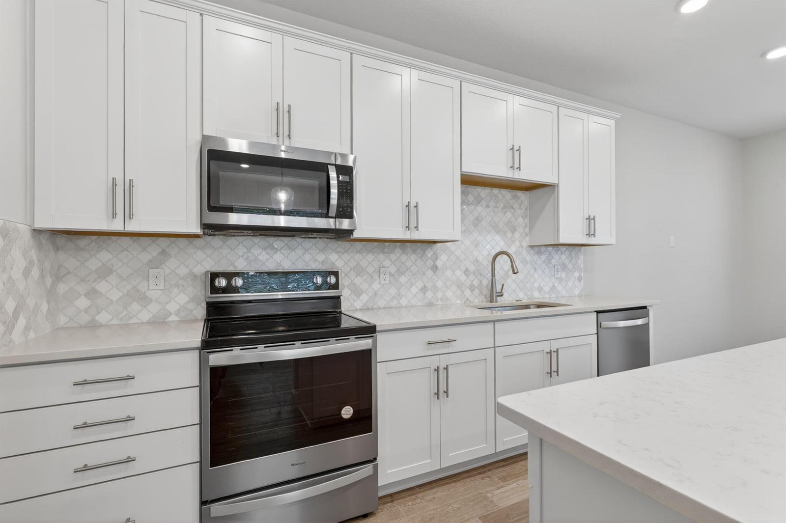 A modern kitchen features white shaker cabinets, stainless steel appliances, and a patterned tile backsplash — 1887 SE Ocean Cove Way, Stuart FL 34996, STUART, FL