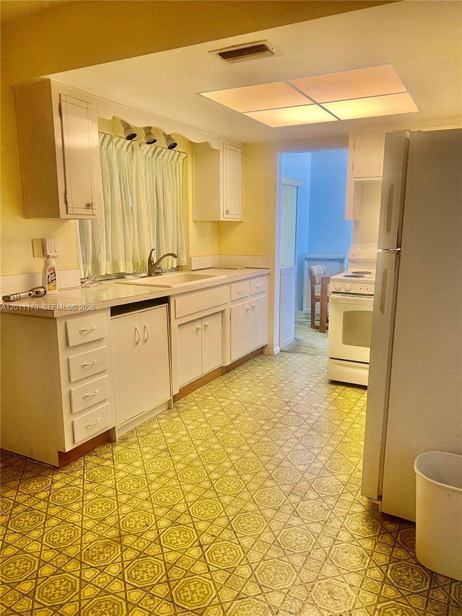 A kitchen features yellow walls, white cabinets, a patterned linoleum floor, and white appliances — 4402 NW 43rd Ter, Tamarac FL 33319, TAMARAC, FL