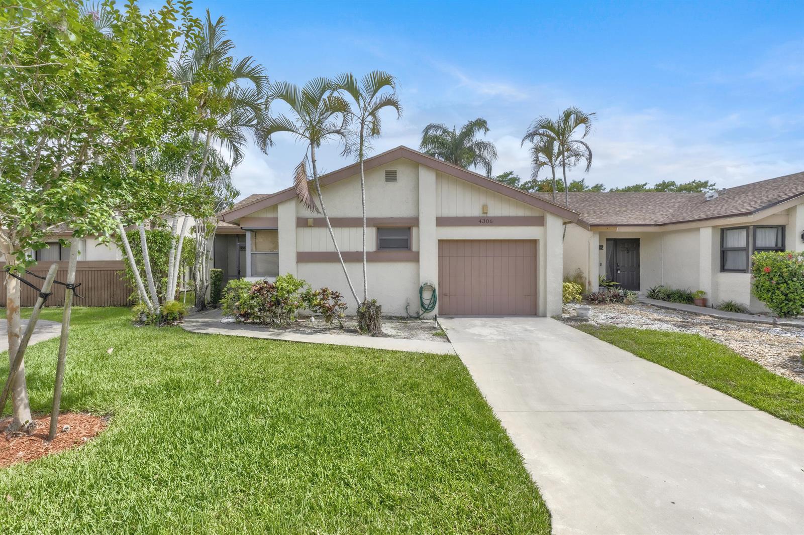 A single-story house with a tan stucco exterior, a brown garage door, and palm trees — 4306 Acacia Circle, Coconut Creek FL 33066, COCONUT CREEK, FL