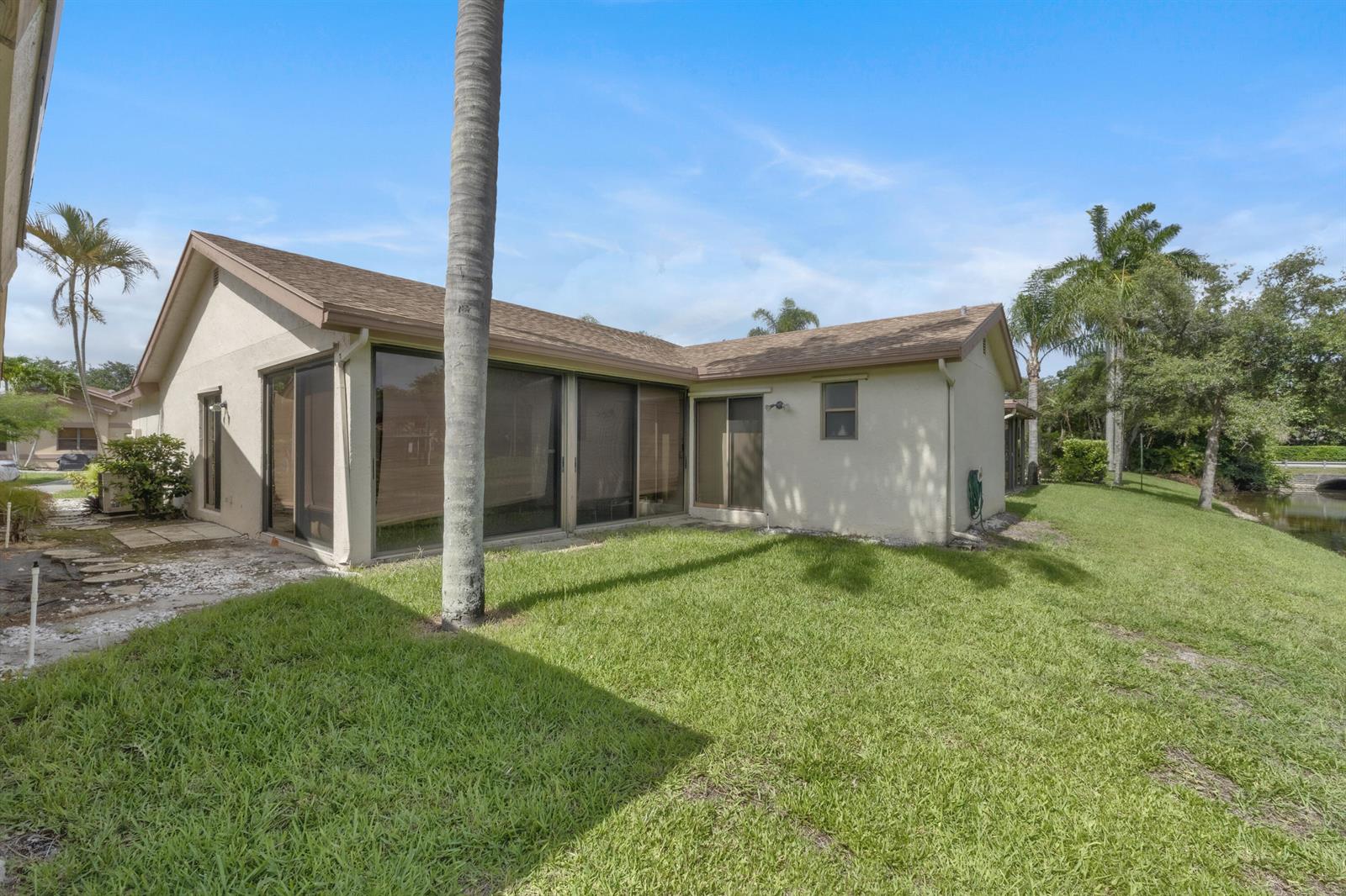 The exterior of a beige house features sliding glass doors and a grassy backyard — 4306 Acacia Circle, Coconut Creek FL 33066, COCONUT CREEK, FL