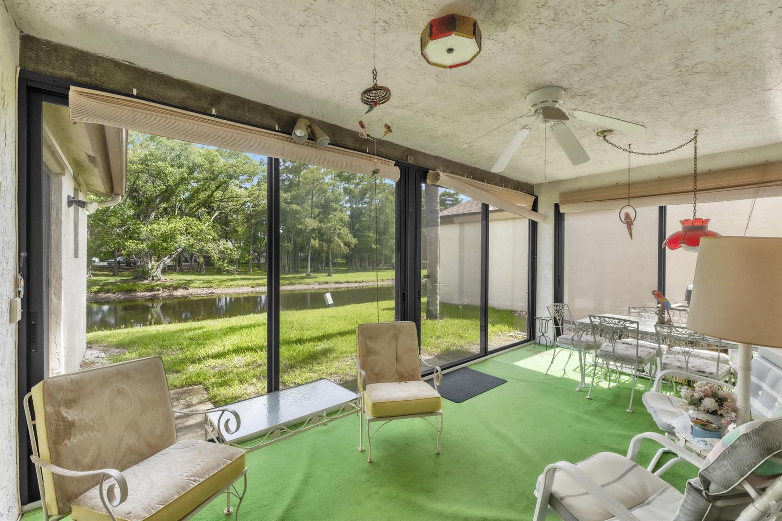 A sunroom with green carpet, white furniture, and large windows overlooking a grassy pond area — 4306 Acacia Circle, Coconut Creek FL 33066, COCONUT CREEK, FL