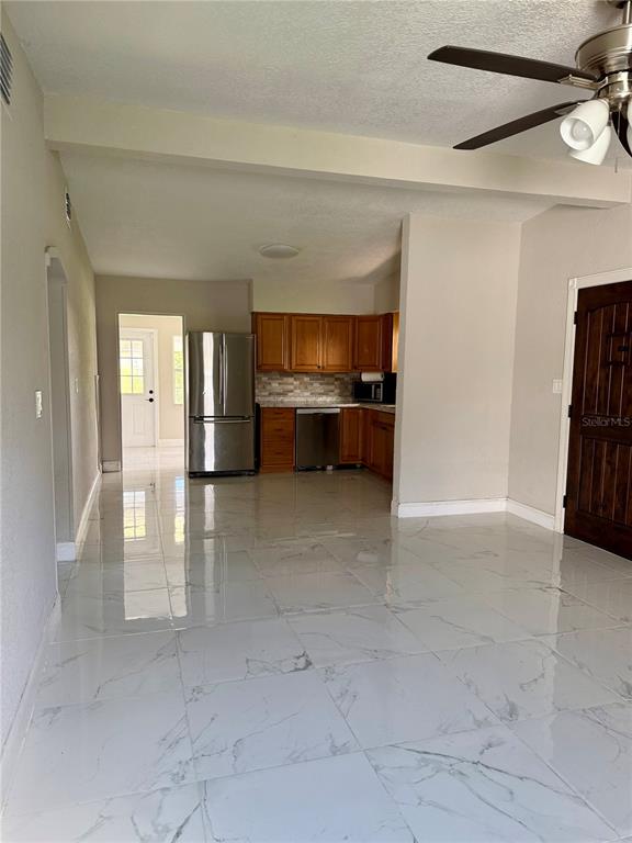 A kitchen with wooden cabinets and stainless steel appliances opens to a tiled living area — 1601 ROSELAWN STREET SW, WINTER HAVEN, FL