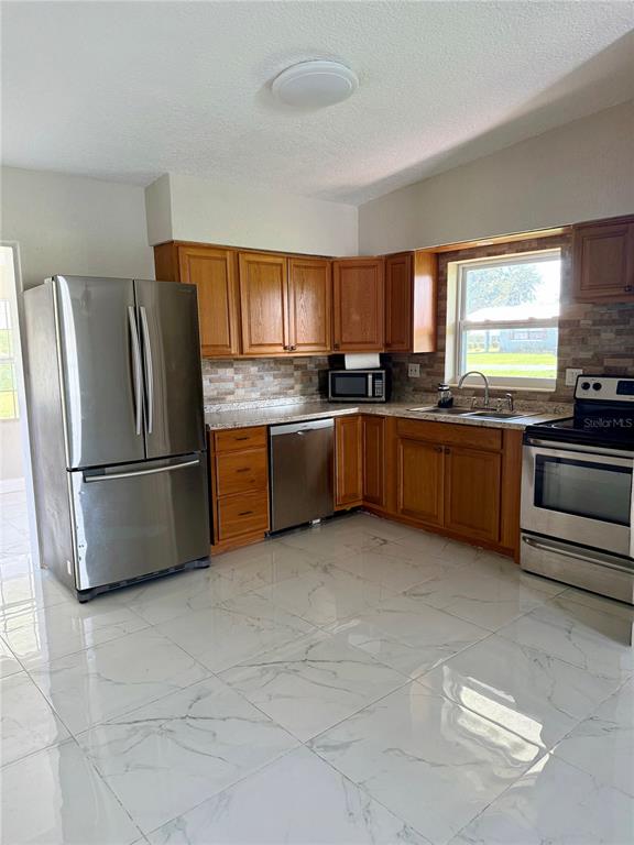 A kitchen features stainless steel appliances, wood cabinets, and white marble-patterned tile flooring — 1601 ROSELAWN STREET SW, WINTER HAVEN, FL