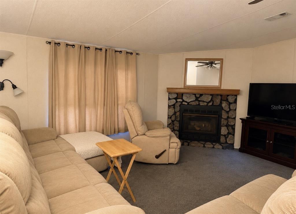 A living room features a stone fireplace, beige sofa, recliner, and tan curtains — 794 NE 521 STREET, OLD TOWN, FL