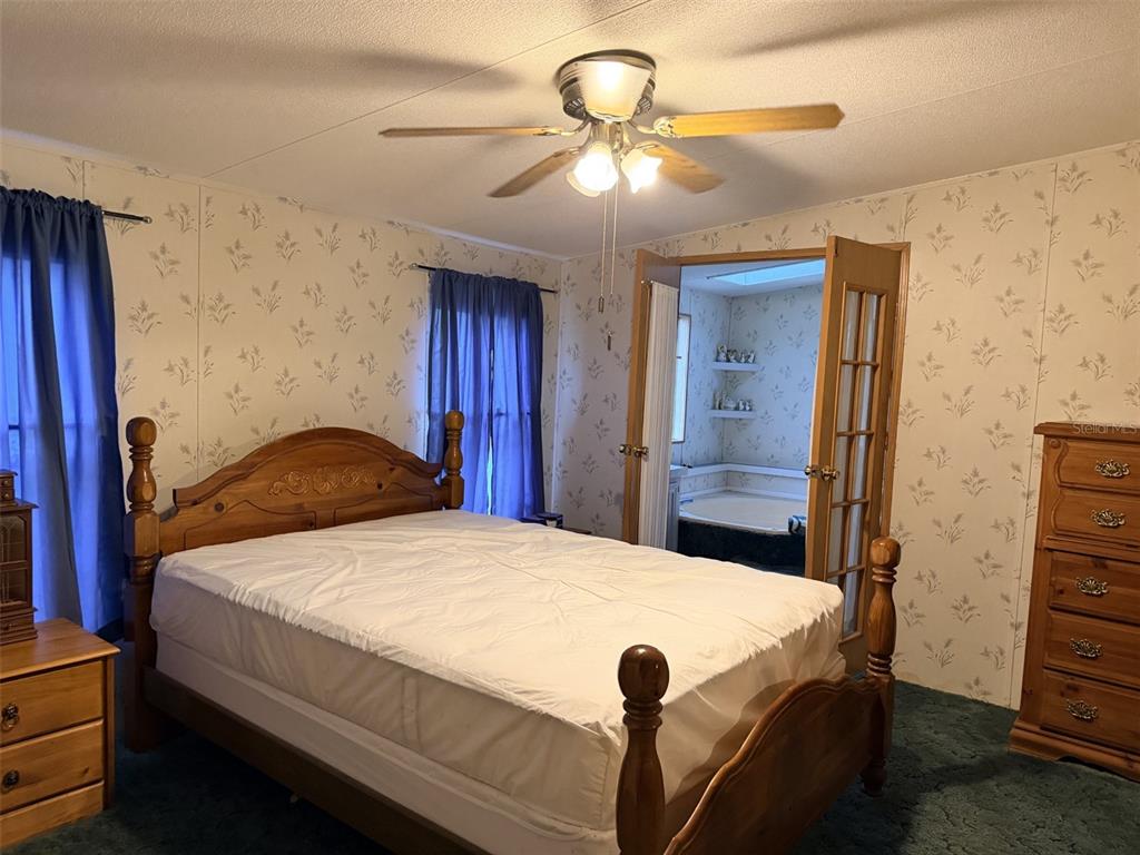 A bedroom with floral wallpaper, a wooden bed frame, green carpet, and an attached bathroom — 794 NE 521 STREET, OLD TOWN, FL