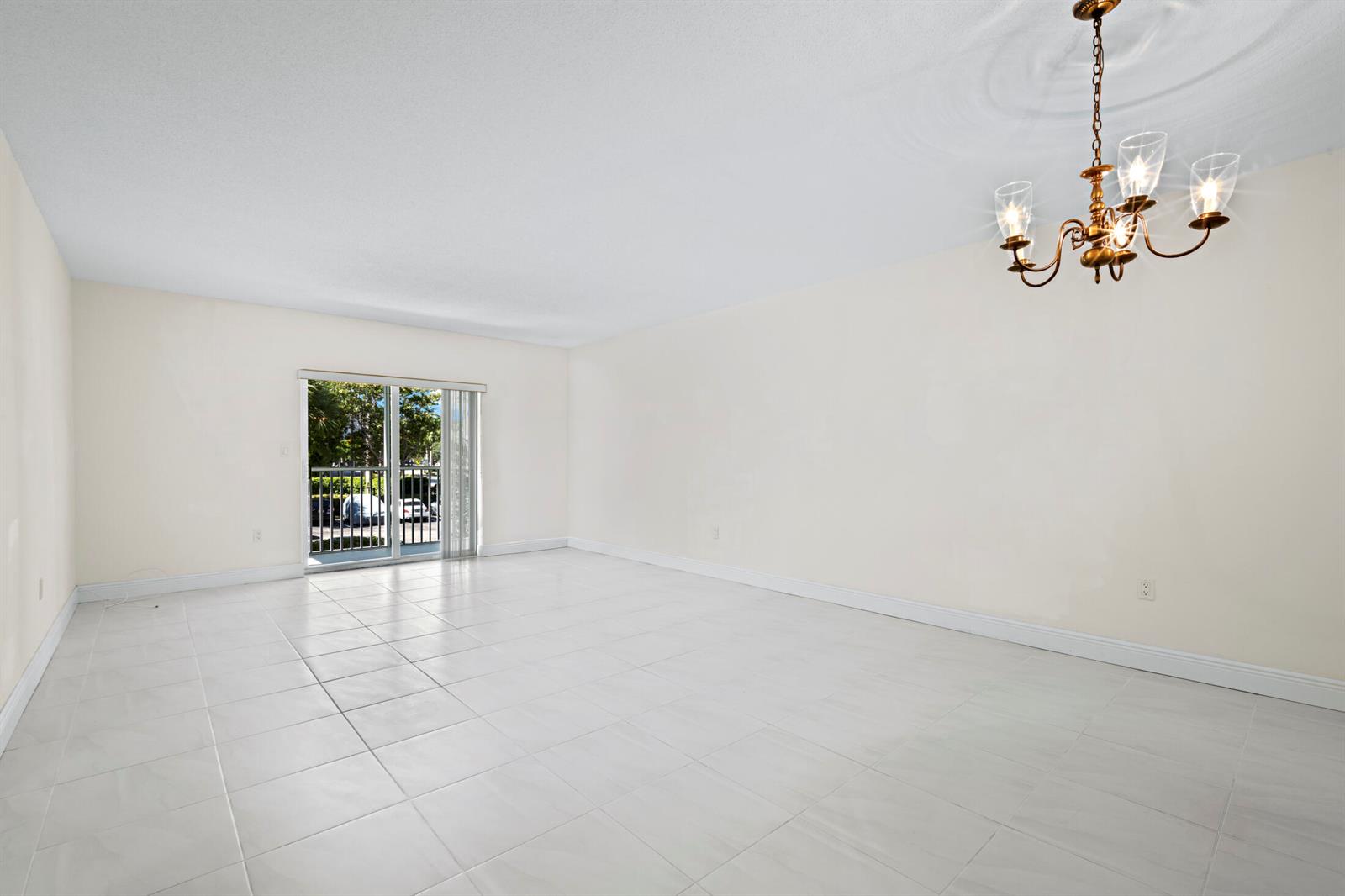 An empty room with white tile flooring, plain walls, a chandelier, and a sliding glass door — 200 E Royal Palm Road # 2110, Boca Raton FL 33432, BOCA RATON, FL