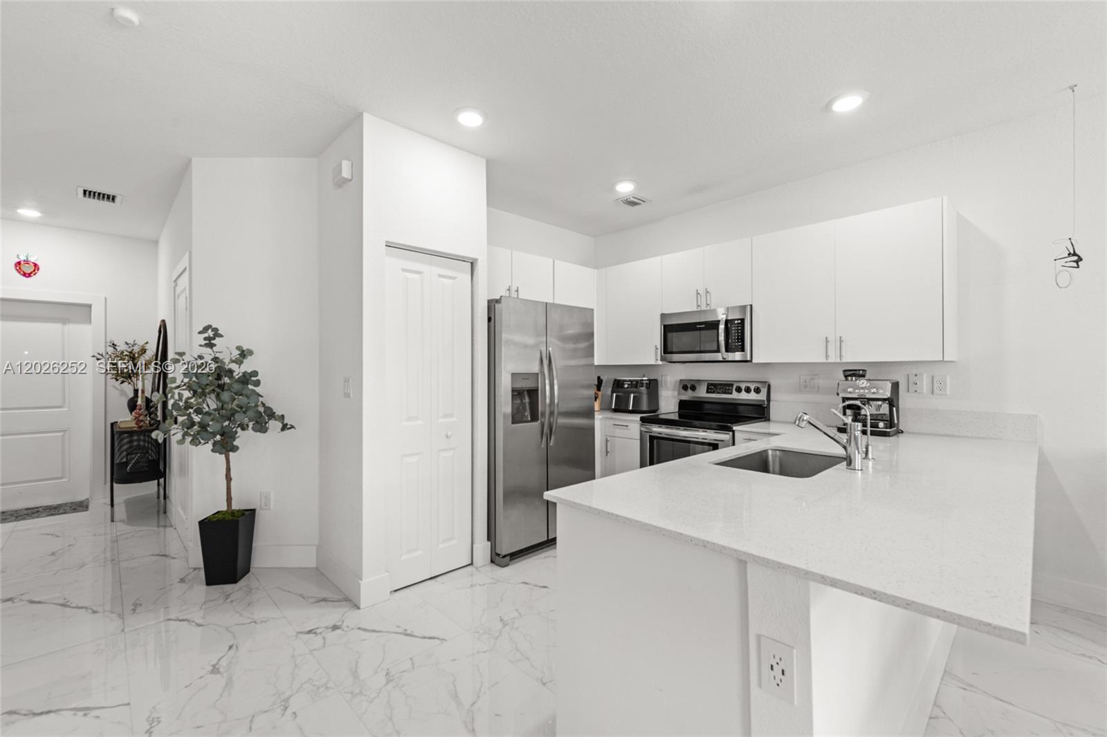 A modern kitchen features white cabinets, stainless steel appliances, and white marble-patterned tile flooring — 577 NW 204th St, Miami Gardens FL 33169, MIAMI GARDENS, FL