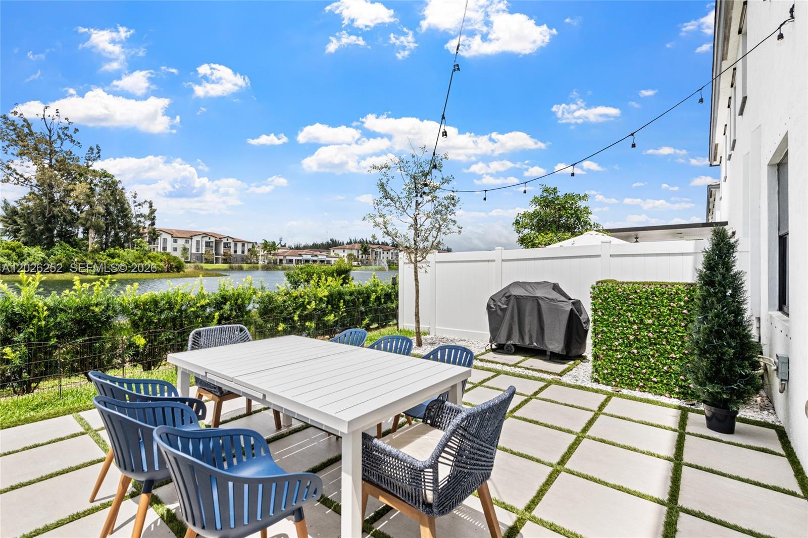A patio features a white dining table with blue chairs, a grill, and a lake view — 577 NW 204th St, Miami Gardens FL 33169, MIAMI GARDENS, FL