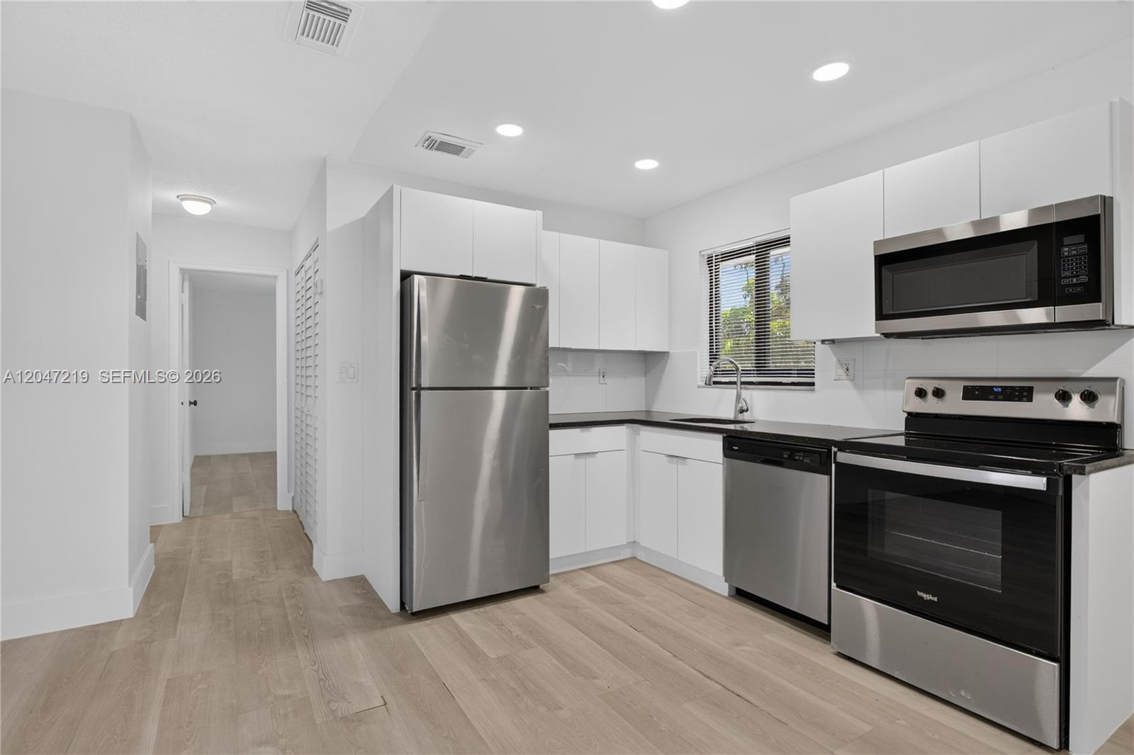 A modern kitchen features white cabinets, stainless steel appliances, and light wood-look flooring — 615 NE 26TH ST # 7, Wilton Manors FL 33305, WILTON MANORS, FL