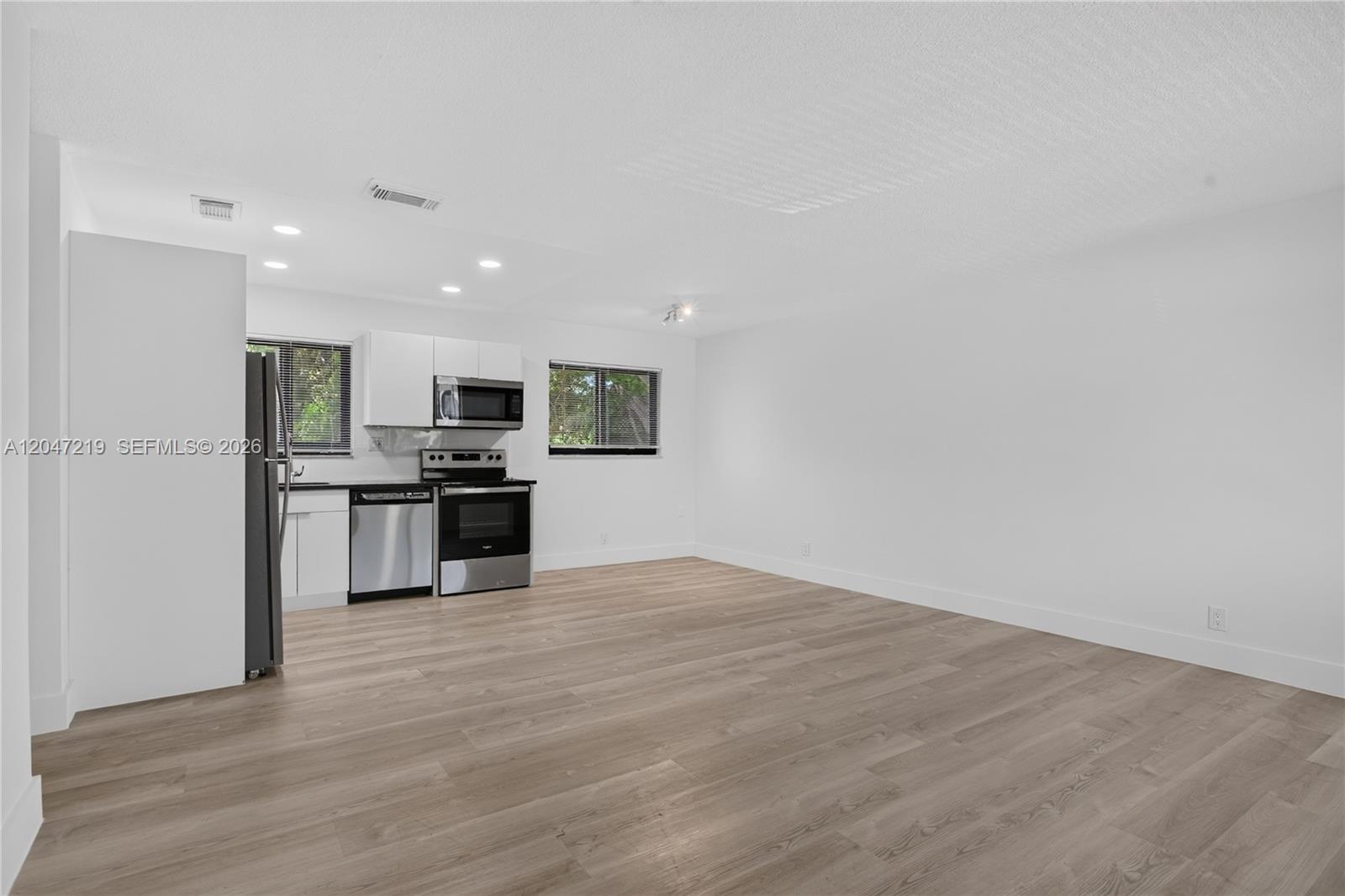 A kitchen with white cabinets and stainless steel appliances opens into a spacious living area — 615 NE 26TH ST # 7, Wilton Manors FL 33305, WILTON MANORS, FL