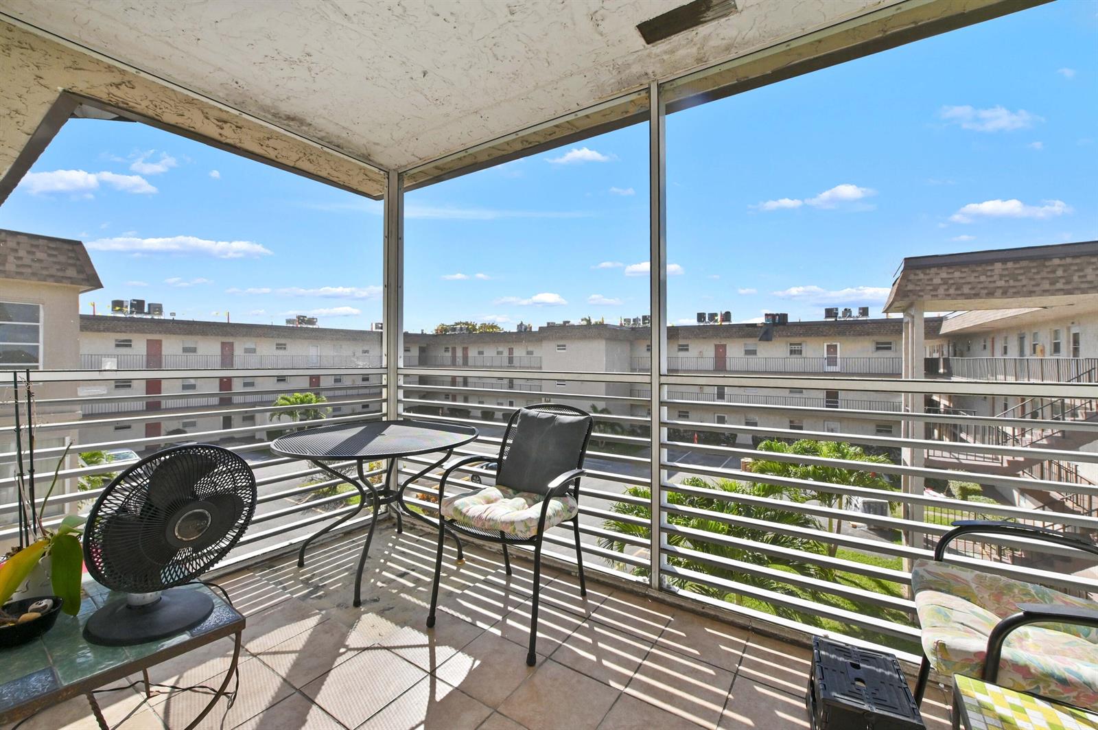 A screened-in balcony with tiled flooring, patio furniture, and a view of apartment buildings — 721 Lori Drive # 313, Palm Springs FL 33461, PALM SPRINGS, FL
