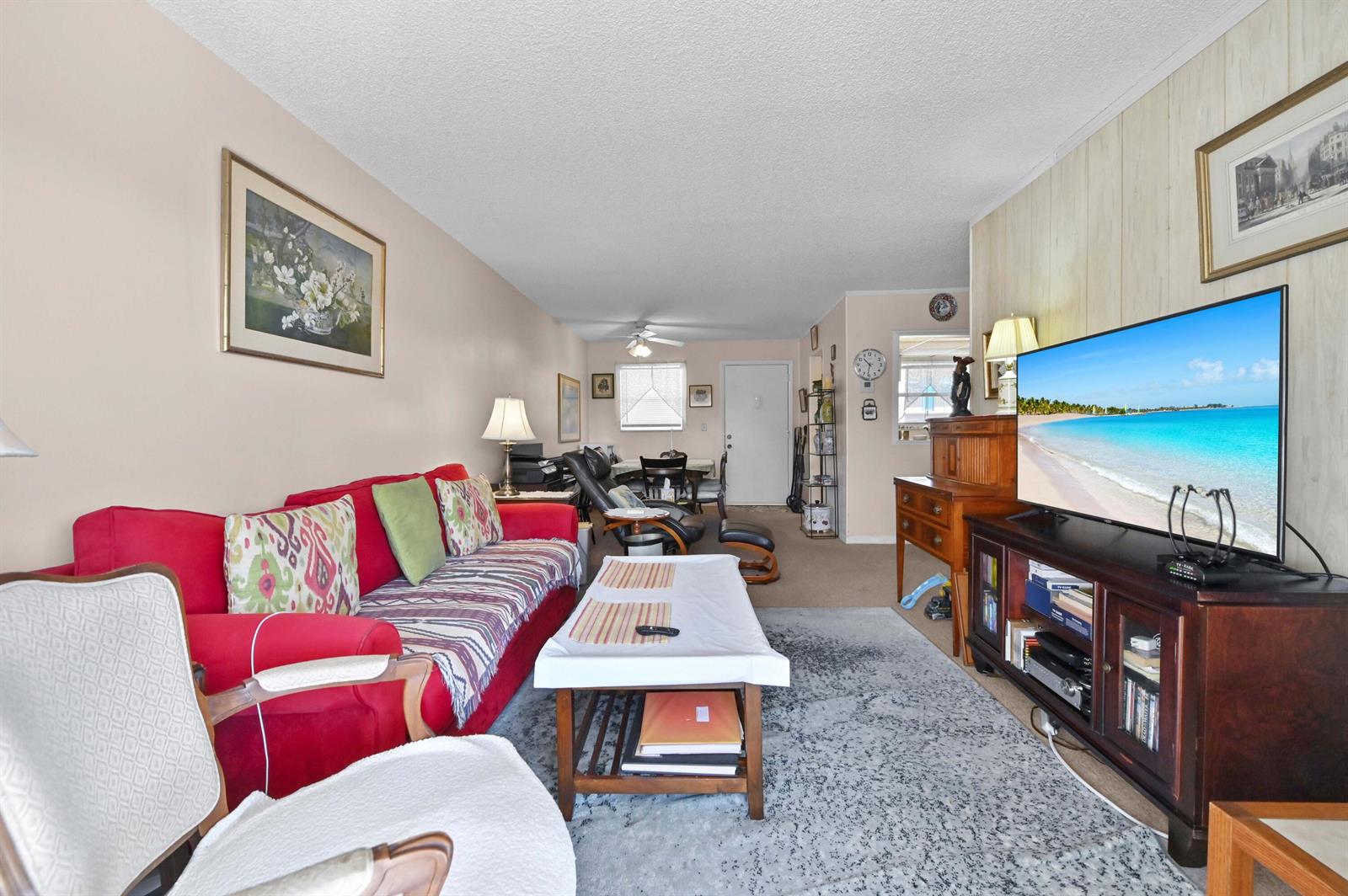A living room features a red sofa, a television on a wooden stand, and carpet — 721 Lori Drive # 313, Palm Springs FL 33461, PALM SPRINGS, FL