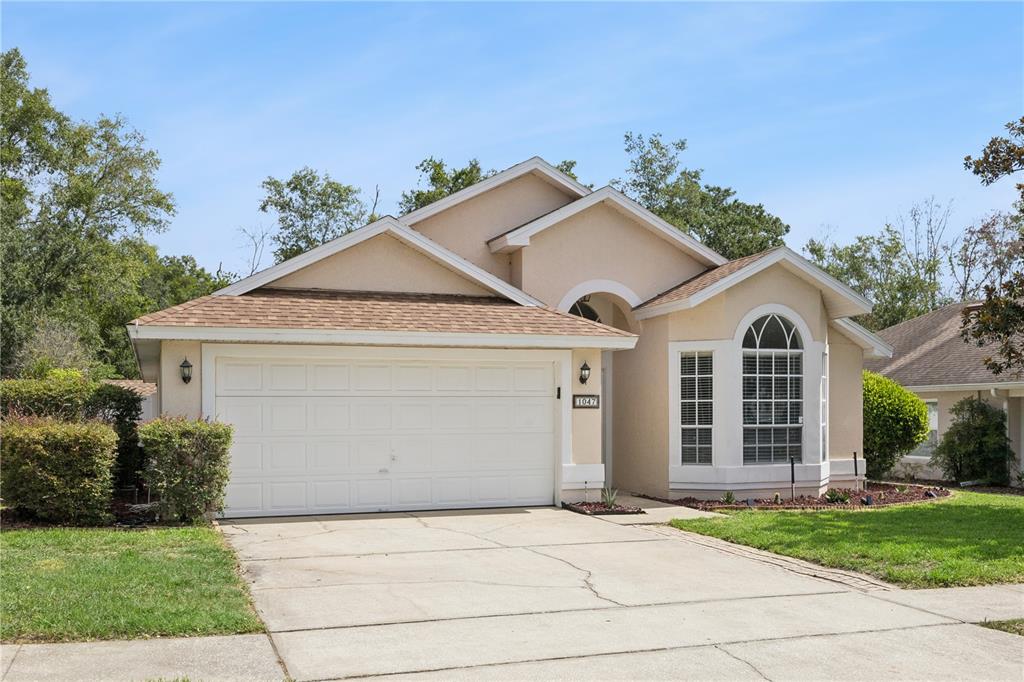 A single-story suburban house with a beige stucco exterior, a two-car garage, and arched windows — 1047 ROYAL OAKS DRIVE, APOPKA, FL