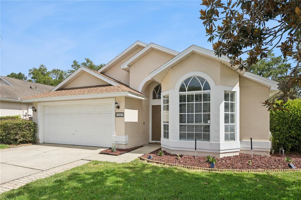 A single-story house with a beige stucco exterior, a two-car garage, and a bay window — 1047 ROYAL OAKS DRIVE, APOPKA, FL