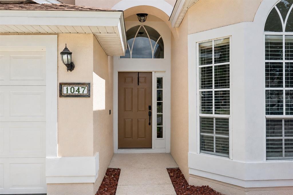 The exterior entrance features a brown front door, a house number plaque, and arched windows — 1047 ROYAL OAKS DRIVE, APOPKA, FL