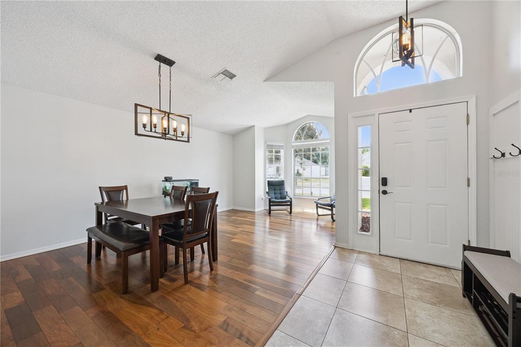 A dining area with wood floors transitions to a tiled entryway with a white front door — 1047 ROYAL OAKS DRIVE, APOPKA, FL