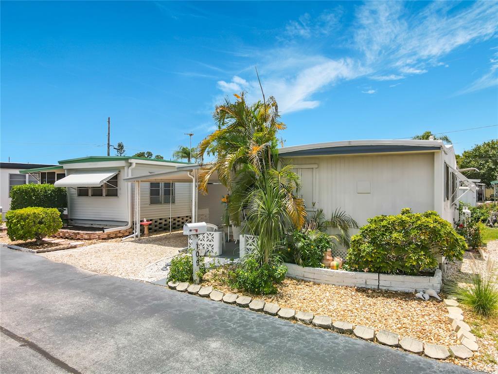 A single-story mobile home features a carport, gravel landscaping, and a palm tree — 7490 46TH AVENUE N UNIT 109, ST PETERSBURG, FL