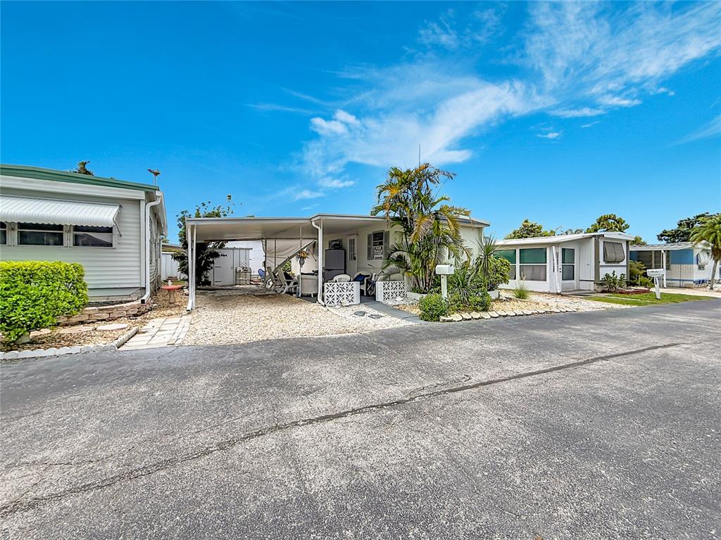 A mobile home with a carport and gravel driveway sits under a bright blue sky — 7490 46TH AVENUE N UNIT 109, ST PETERSBURG, FL